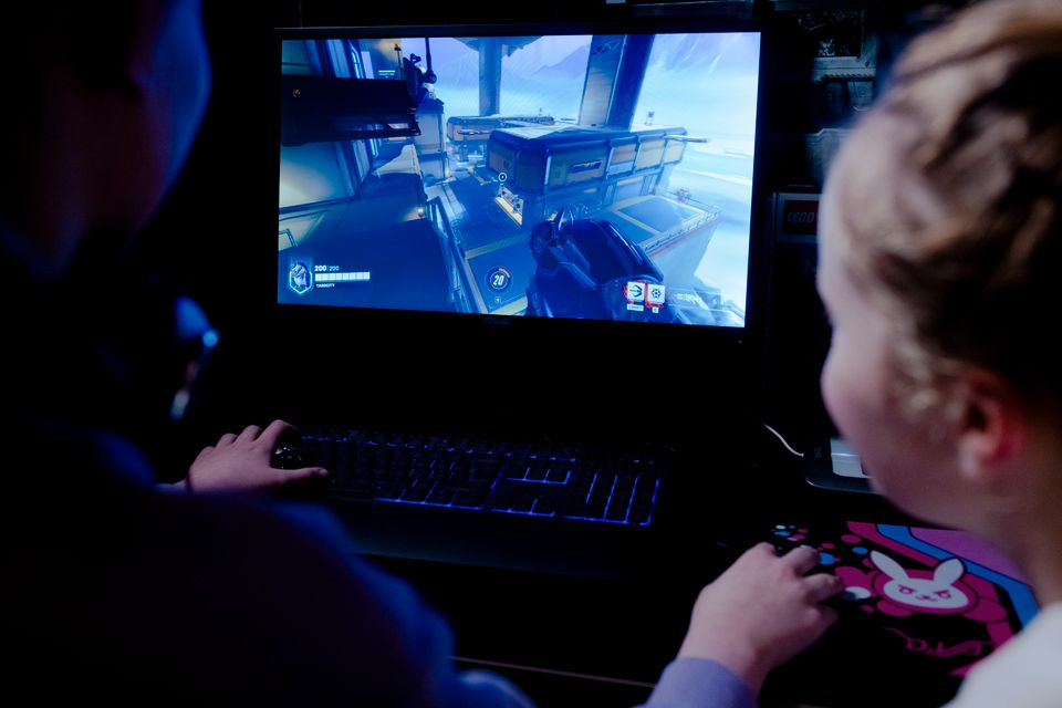 Nærbilde av to jenter bakfra som sitter foran en PC og spiller et skytespill.