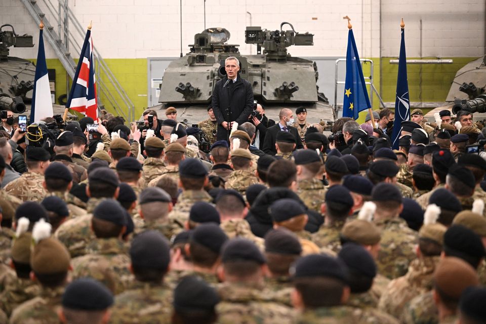 En dresskledd mann med grått hår står på et podie og snakker foran en stor gruppe med kamuflasje-kledde soldater.