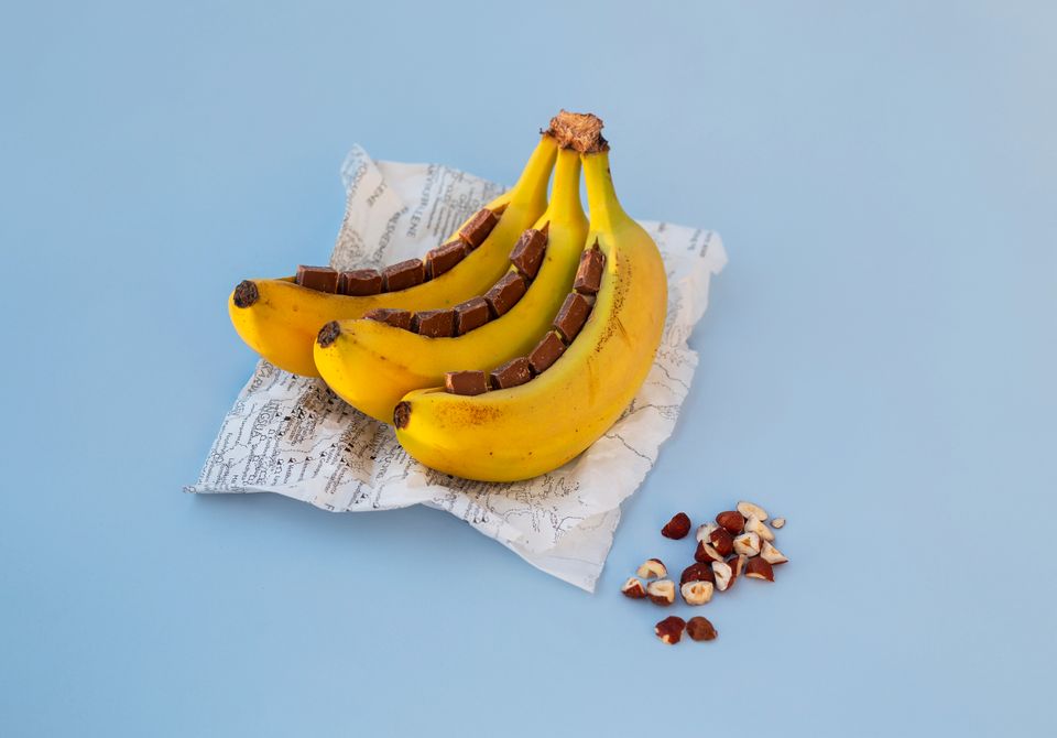 En klase med tre bananer ligger på et matpapir med turkart trykket på, og hver banan er snittet opp og sjokoladebiter er trykket ned i snittet.