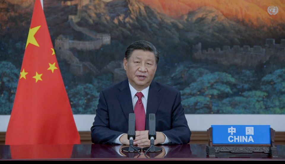 Kinas president sitter ved et skrivebord med et kinesisk flagg på siden og snakker inn i mikrofoner. 