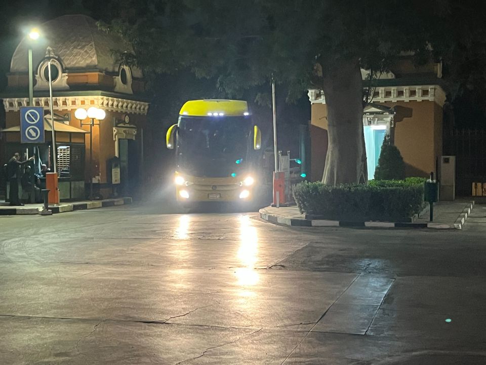 En gul buss kjører inn på en parkeringsplass mens frontlyktene lyser opp i mørket