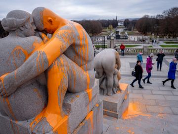En grå statue av to mennesker som holder rundt hverandre har oransje maling over seg.