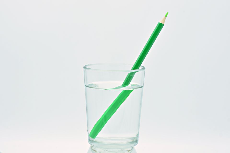 Bildet viser et vannglass med en grønn blyant i, som ser knekt ut, mot en hvit bakgrunn.