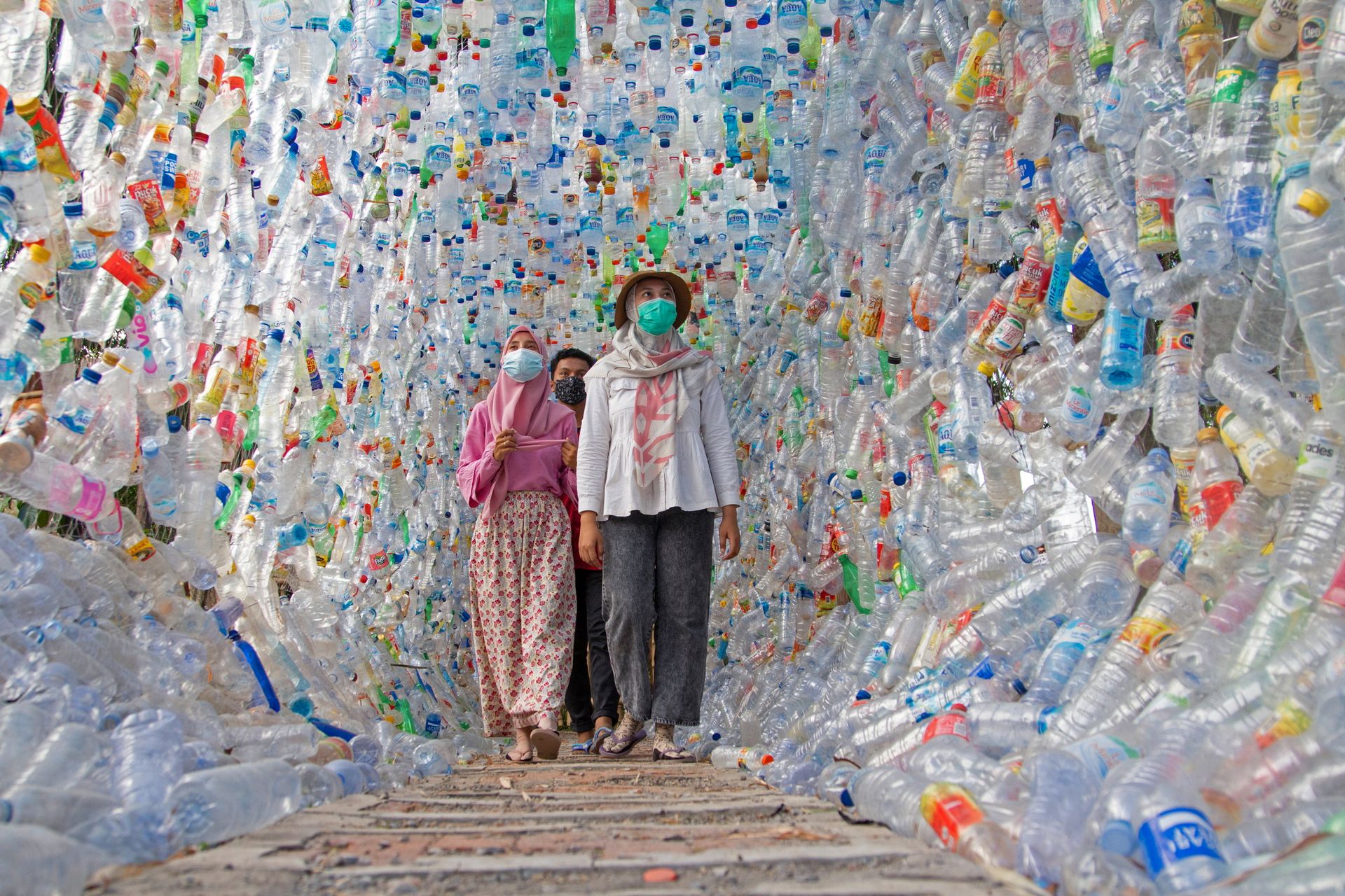 Tre personer går i en tunnel laget av plastflasker.