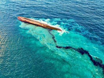 Et stort, rødt skip er opp ned i vannet og bak fra båten renner det ut olje.
