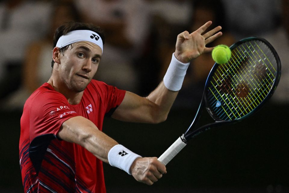 En tennisspiller med rød t-skjorte og hvitt pannebånd slår en ball.