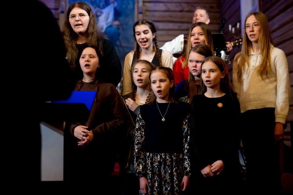 En gruppe barn og ungdommer står foran i en kirke og synger. De er pyntet og følger med på dirigenten.