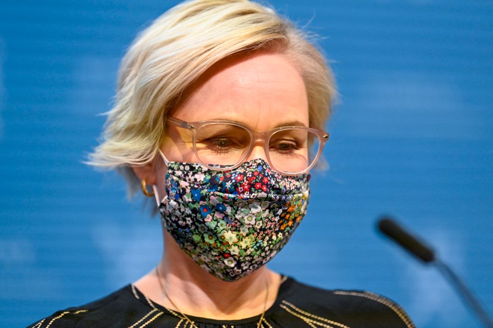 En alvorlig politiker med fargerikt munnbind står foran en mikrofon.