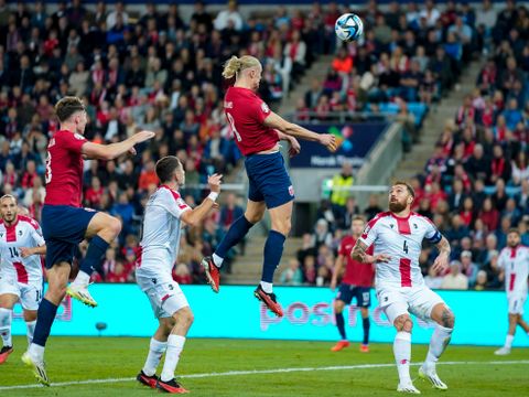 Flere fotballspillere, den ene med rød drakt og langt, lyst hår hopper høyt i luften og er i ferd med å heade ballen.