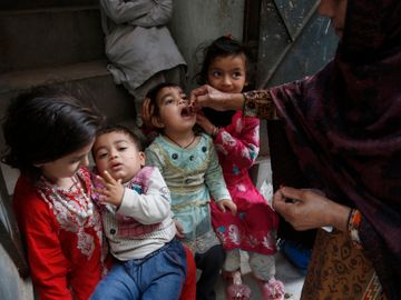 Fire unge barn med fargerike klær får en poliovaksine dryppet inn i munnen fra en voksen kvinne med burka på.
