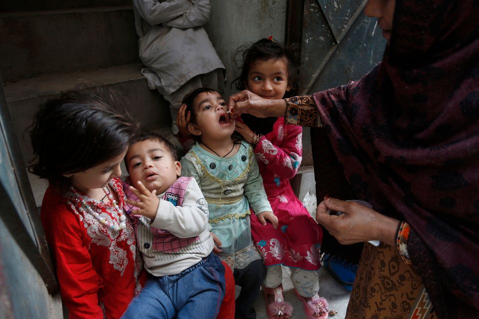 Fire unge barn med fargerike klær får en poliovaksine dryppet inn i munnen fra en voksen kvinne med burka på.