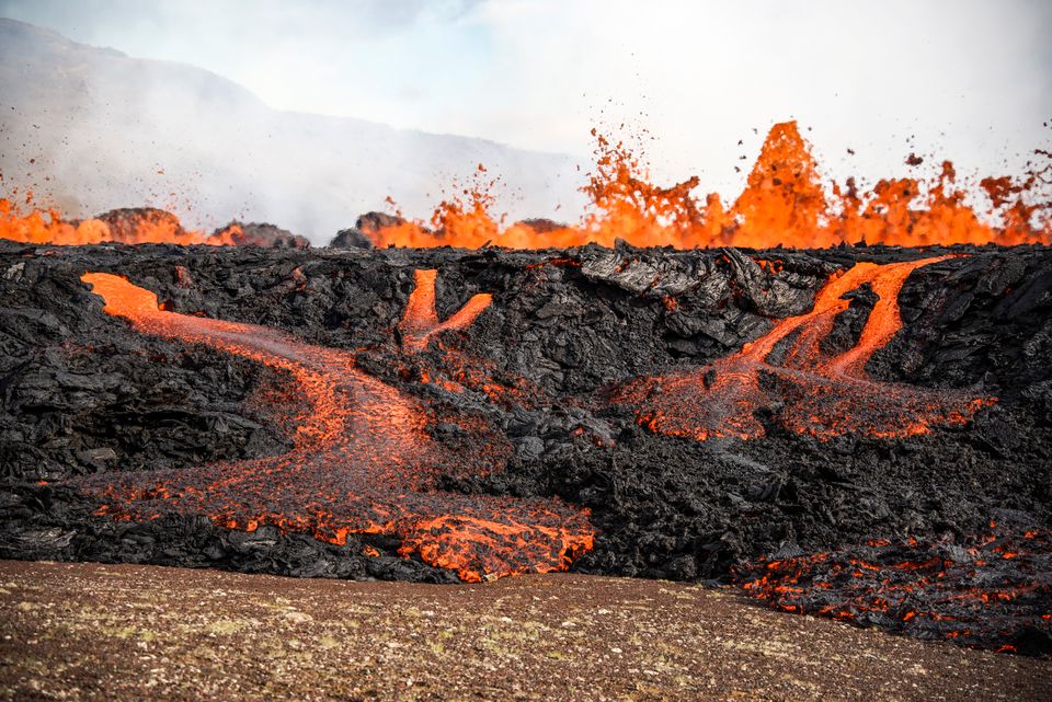 Glødende lava spruter opp fra en vulkan med masse svart stein og sot rundt