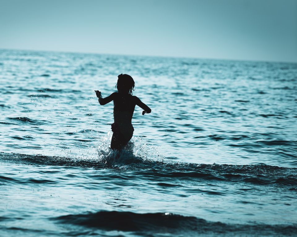 En ung gutt løper gjennom blått vann, som tilsynelatende er kaldt.