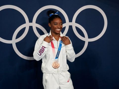 En kvinne med hvite klær og svart hår har en gullmedalje rundt halsen og smiler.