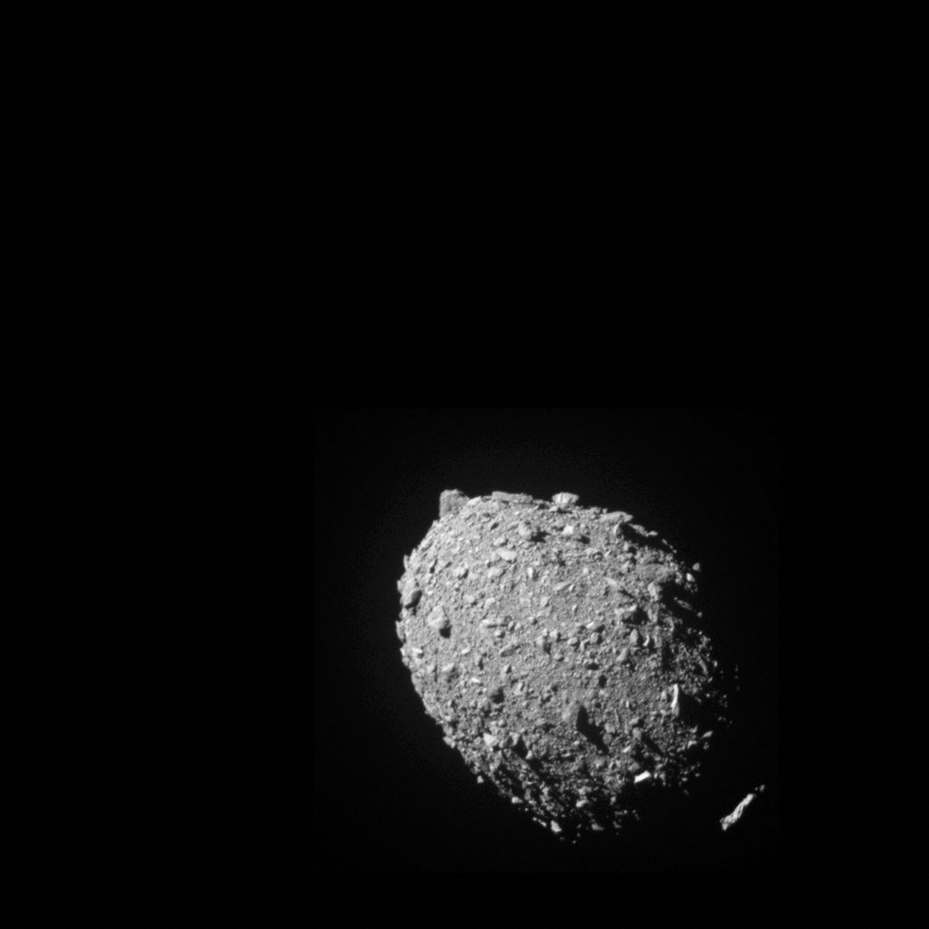 En grå, steinete, rund asteroide ses mot en svart himmel. 