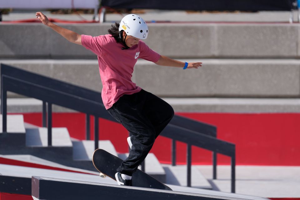 En jente med rosa skjorte og hvit hjelm tar et triks på skateboard.