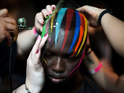 En person uten hår får hodebunnen spraymalt med striper i regnbuens farger.