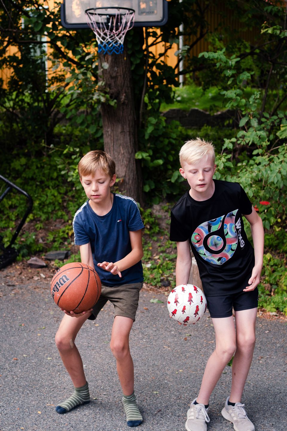 En gutt med brunt hår og en blond gutt holder hver sin ball som de holder på å kaste over skulderen.