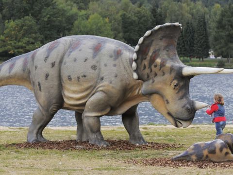 En stor dinosaurusfigur står foran et barn.