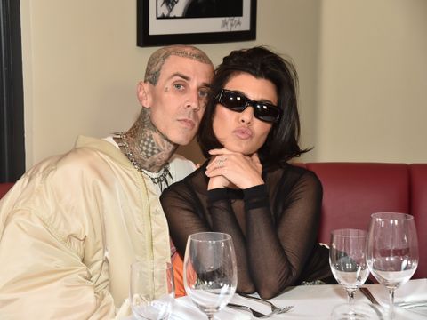 En skallet mann som er dekket av tatoveringer sitter på en restaurant, inntil en kvinne med mørkt hår og solbriller som lager trutmunn til fotografen.