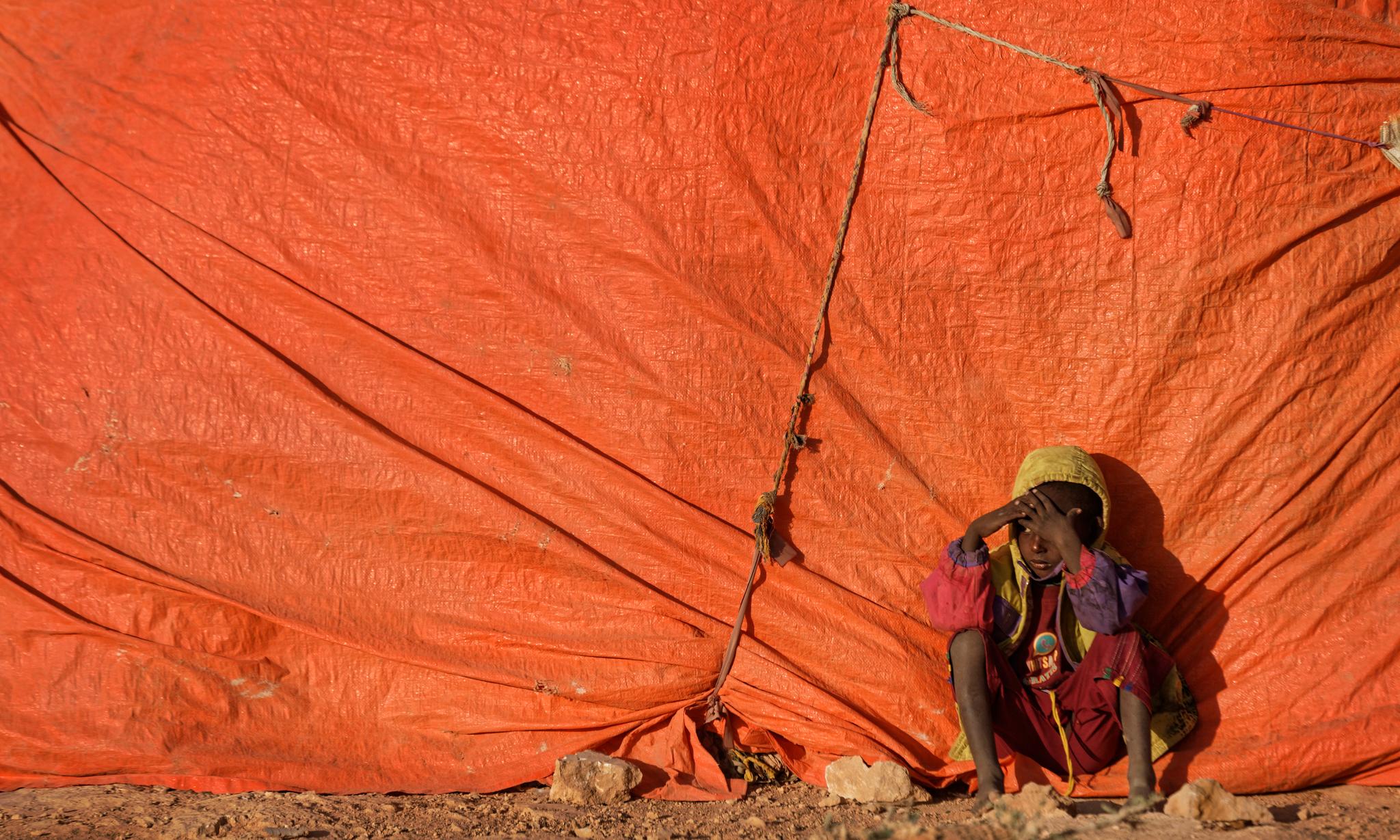 En gutt sitter utenfor et telt i en flyktningleier i Somalia. Her bor mennesker som har måttet flykte på grunn av tørken.