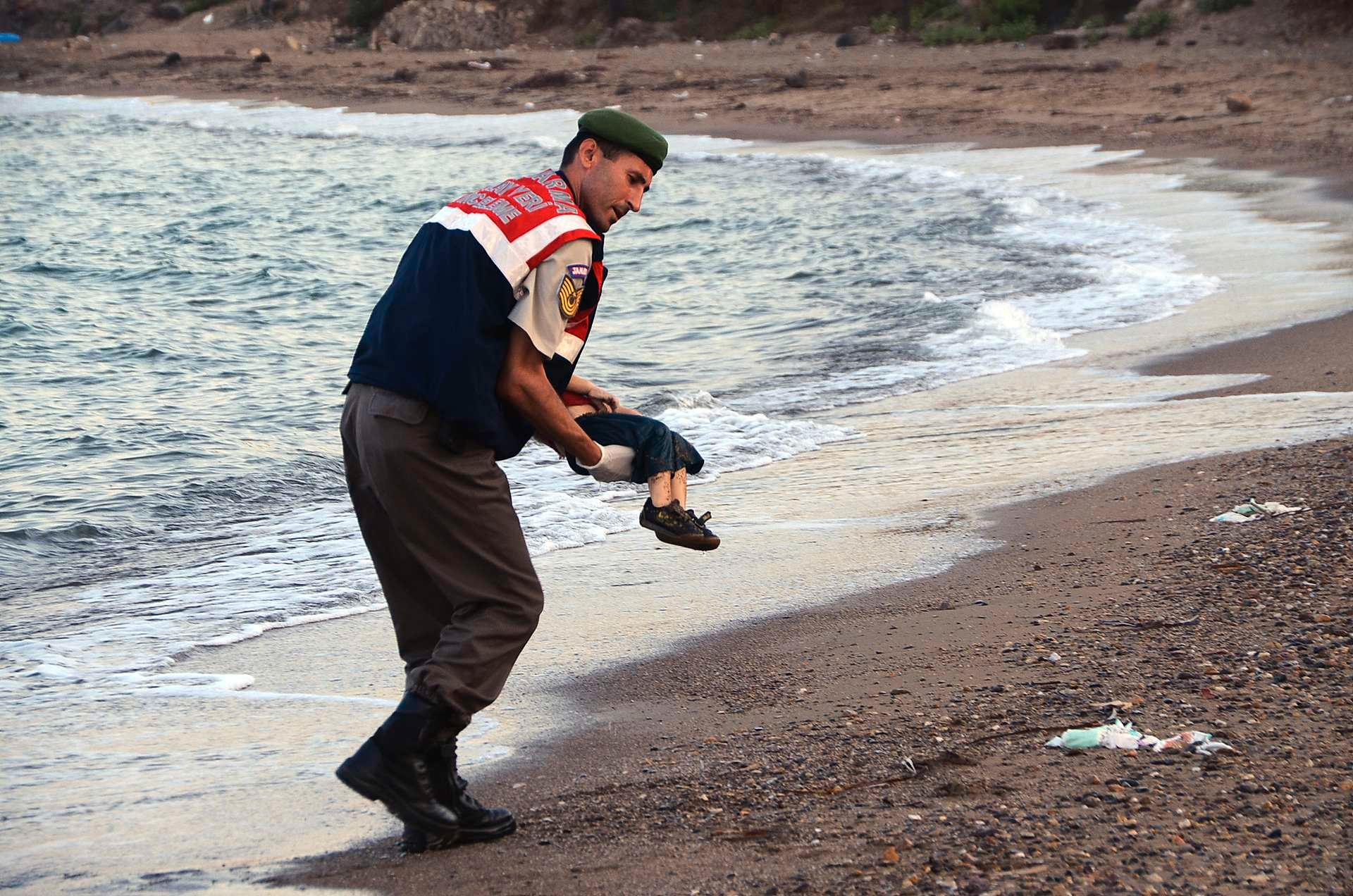 På det aller sterkeste bildet av den døde gutten lå han alene i vannkanten. Her blir han hentet opp av en tyrkisk polititjenestemann. 