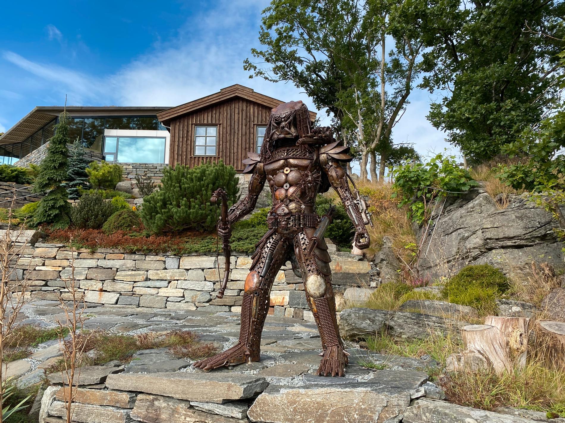 Denne skulpturen har hatt ei lang reise. Frå Thailand, via England til Finnøy. Det er Predator frå filmen Alien, og Merete synes han passar fint på berghylla nedanfor huset.