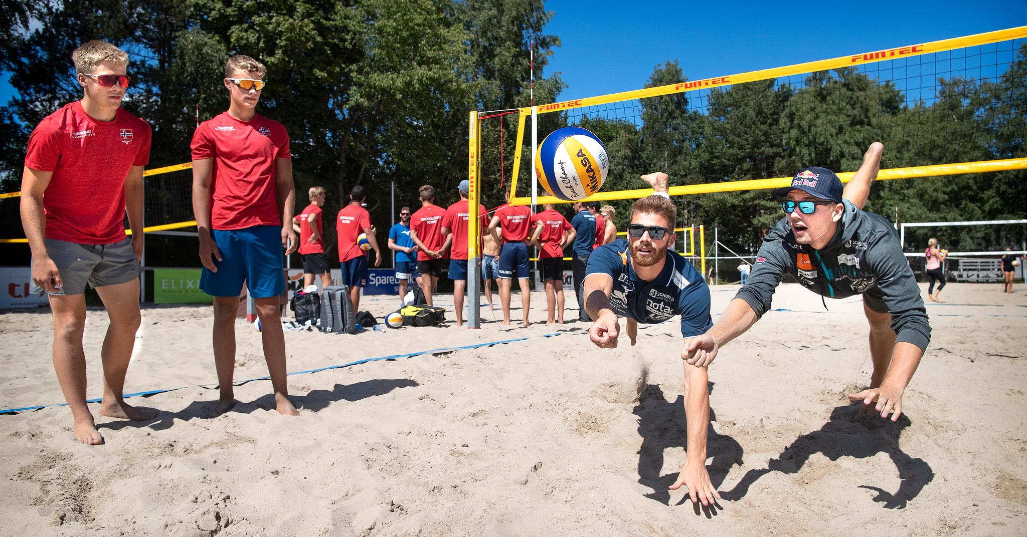 Max Jørgen Fosselie (t.v.) og Even Stray Aas kikker på Anders Mol og Christian Sørum, mens de to verdensenerne lærer bort flere triks og tips til de unge sandvolley-talentene.