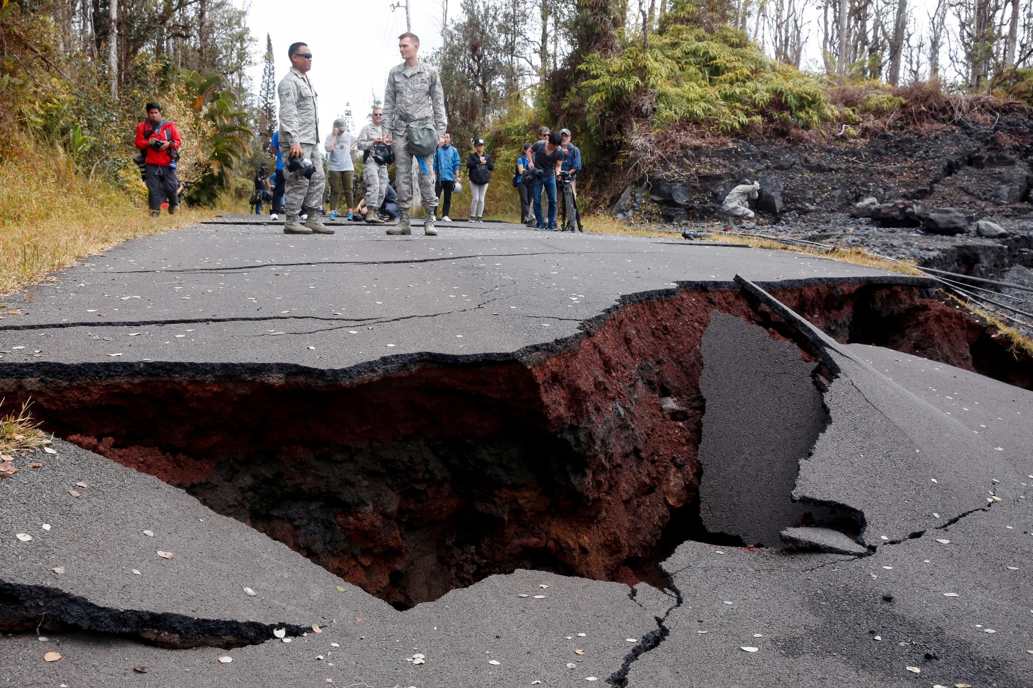 Journalister og soldater fra nasjonalgarden tar en titt på skadene på en vei etter vulkanutbruddet.