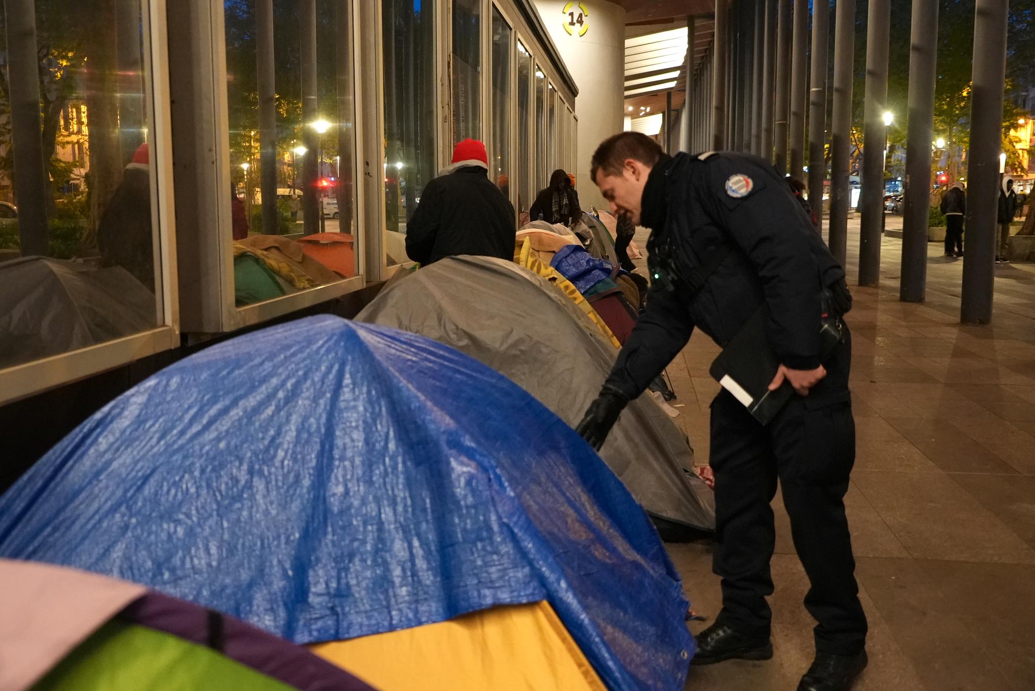  En politimann sjekker innom et telt i en migrantleir i Paris tirsdag morgen. 