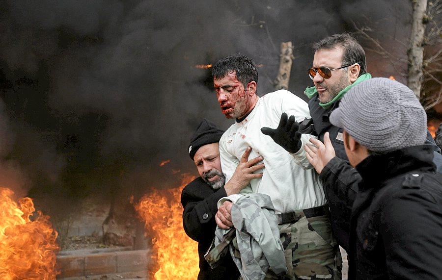 Iranske demonstranter hjelper en politimann i sikkerhet etter at han ble angrepet av voldelige demonstranter under opptøyene 27. desember. FOTO: REUTERS