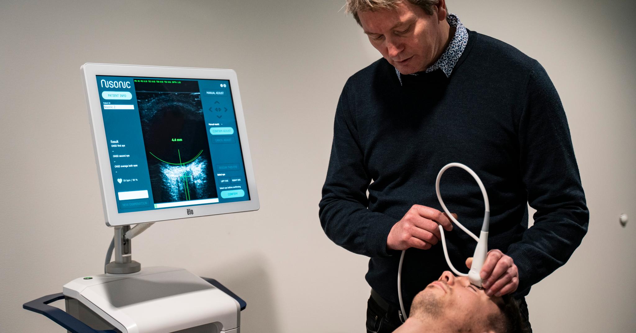 Teknologisjef Tormod Selbekk i Nisonic undersøker  kollega Dag Marius Brurok. Maskinen de utvikler skal lære seg å se alvorlig sykdom som er usynlig for legene. 