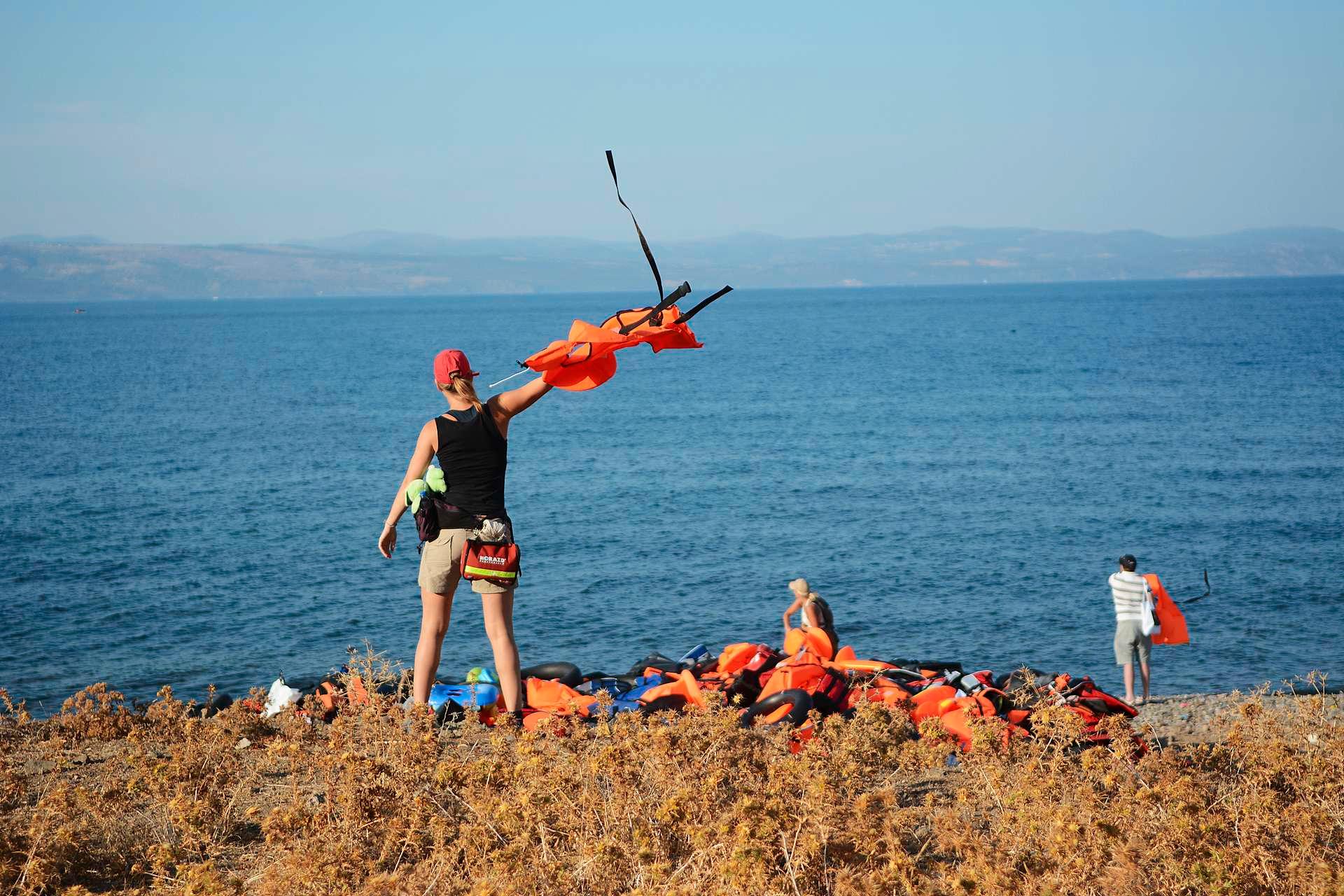 Cecilie Andreassen bruker en av de flere tusen redningsvestene som ligger i hauger langs kysten av Lesbos til å vise flyktningene hvor de bør prøve å styre gummibåten i land. Mange steder er det farlig med skjær i sjøen eller bratte klipper. I bakgrunnen er kysten av Tyrkia.