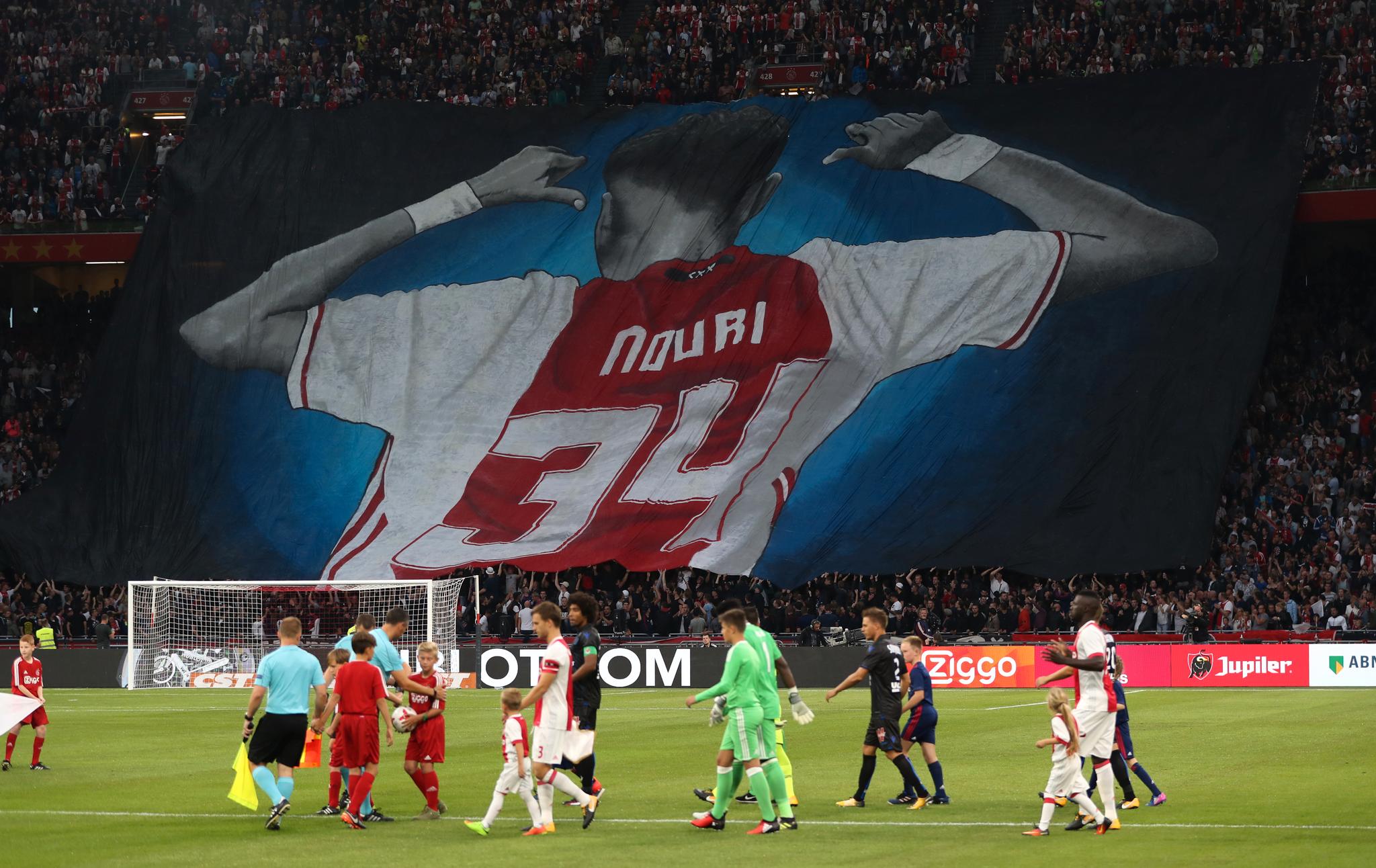 Abdelhak Nouri er lenket fast til sykesengen, men fortsatt er han med Ajax-spillerne i hver eneste kamp. Her løfter supporterne et stort banner av Nouri før en kvalikkamp til Champions League på stadion i Amsterdam. 