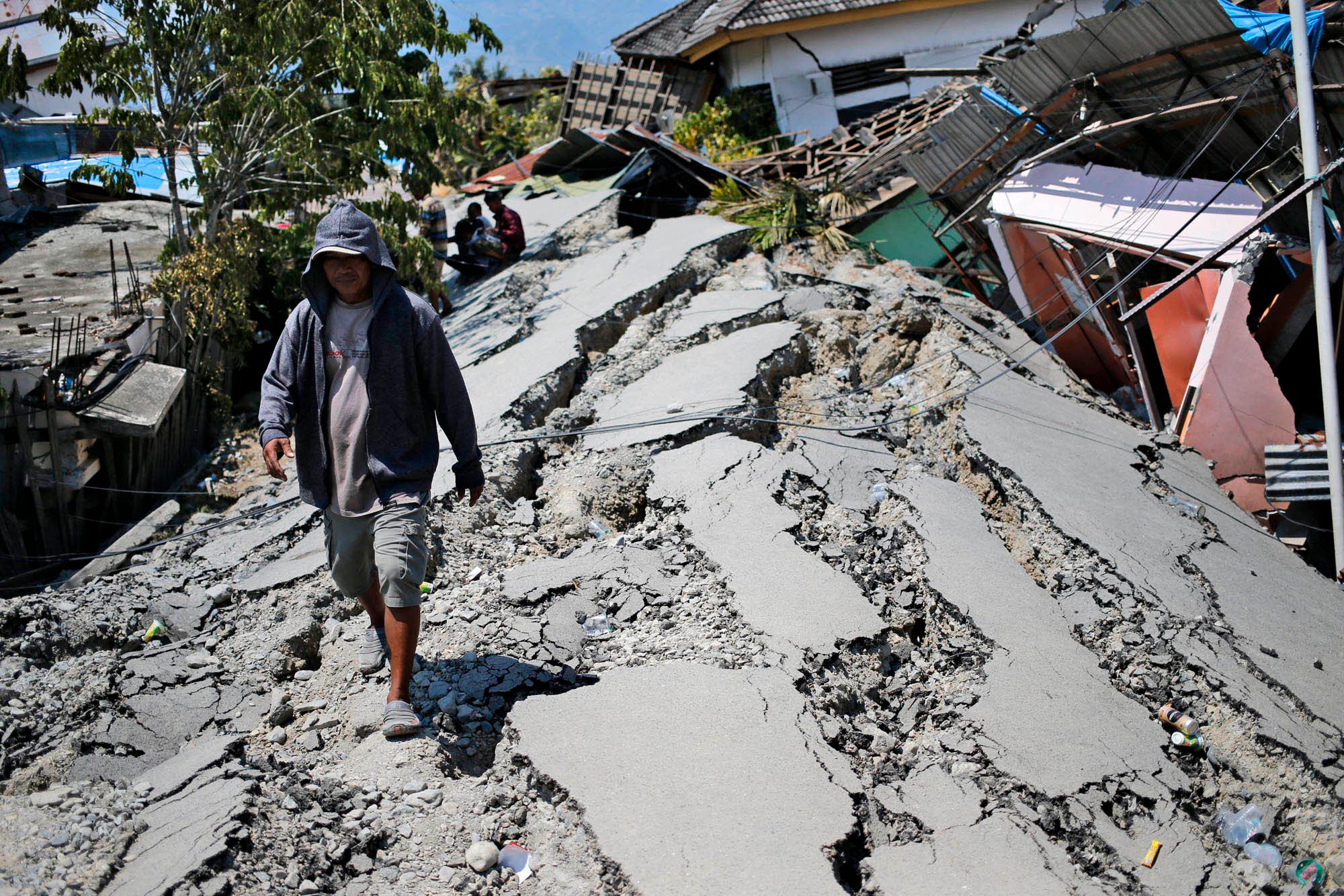En mann går på en svært ødelagt gate i Palu. 