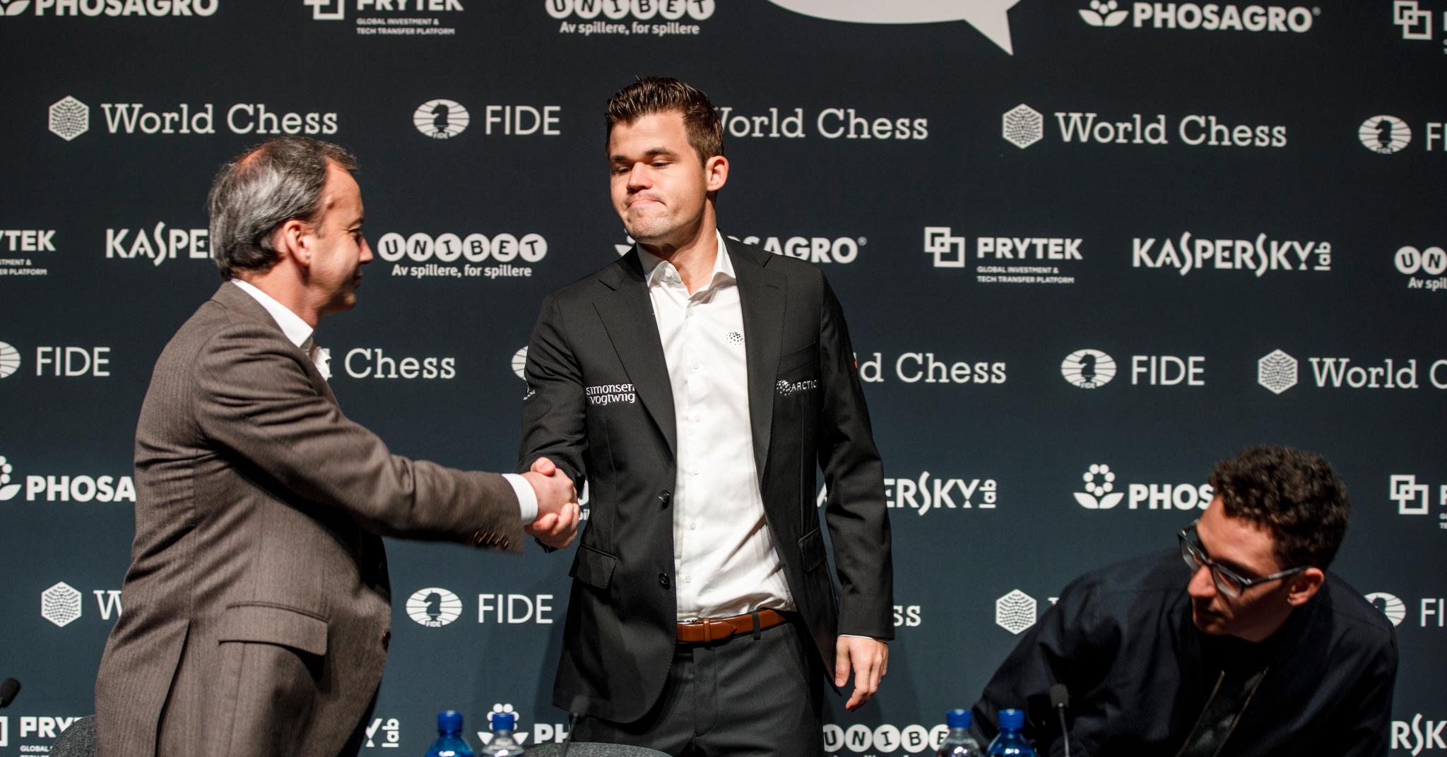 Her hilser Arkadij Dvorkovitsj på Magnus Carlsen og utfordrer Fabiano Caruana før sjakk-VM i 2018. Dvorkovitsj har fått mye ros for jobben han gjør som sjakkpresident, men koblingene til Kreml har gitt ham et forklaringsproblem.