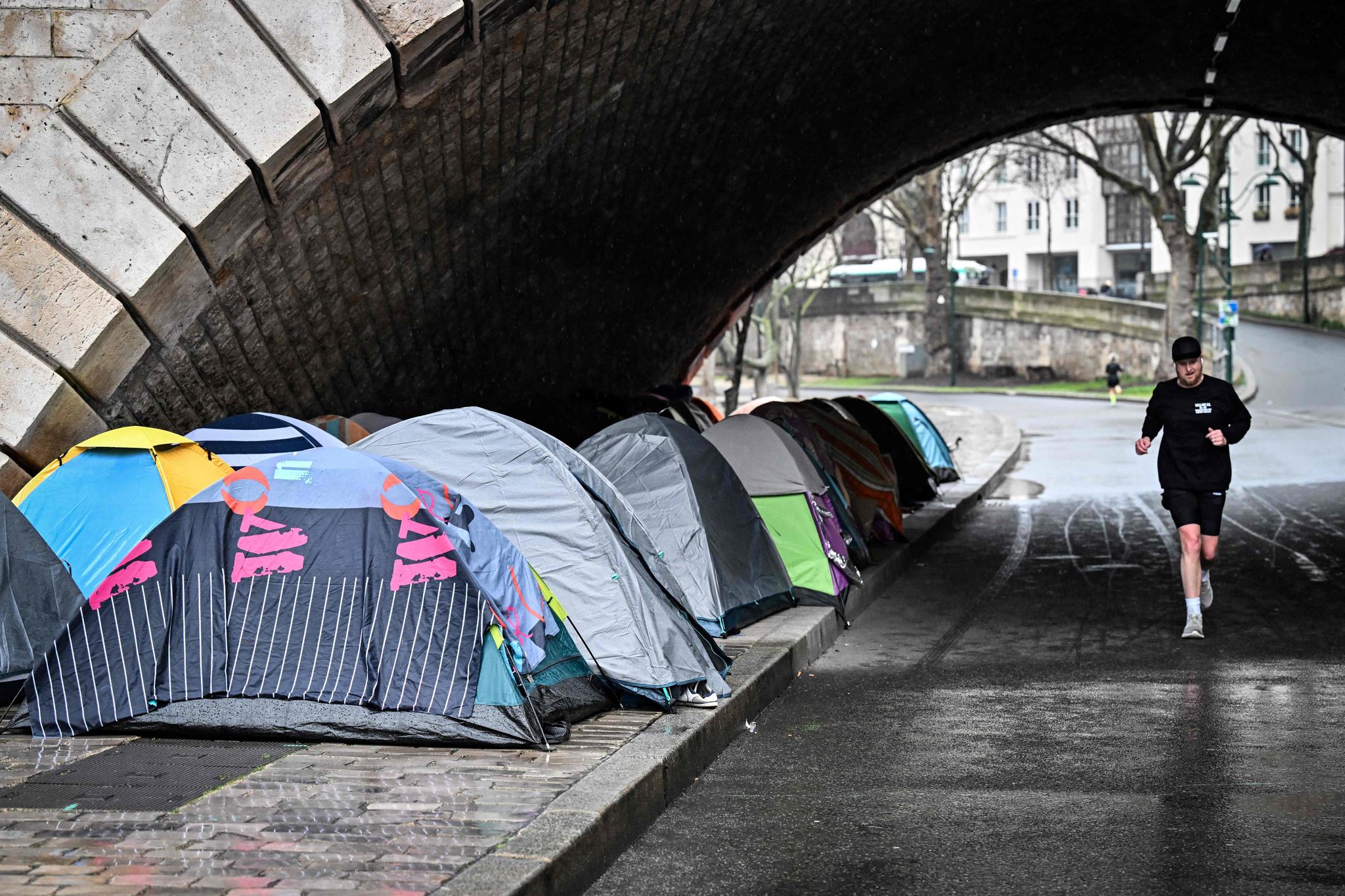 En mann løper forbi telt der hjemløse bor under Sully-broen i Paris.
