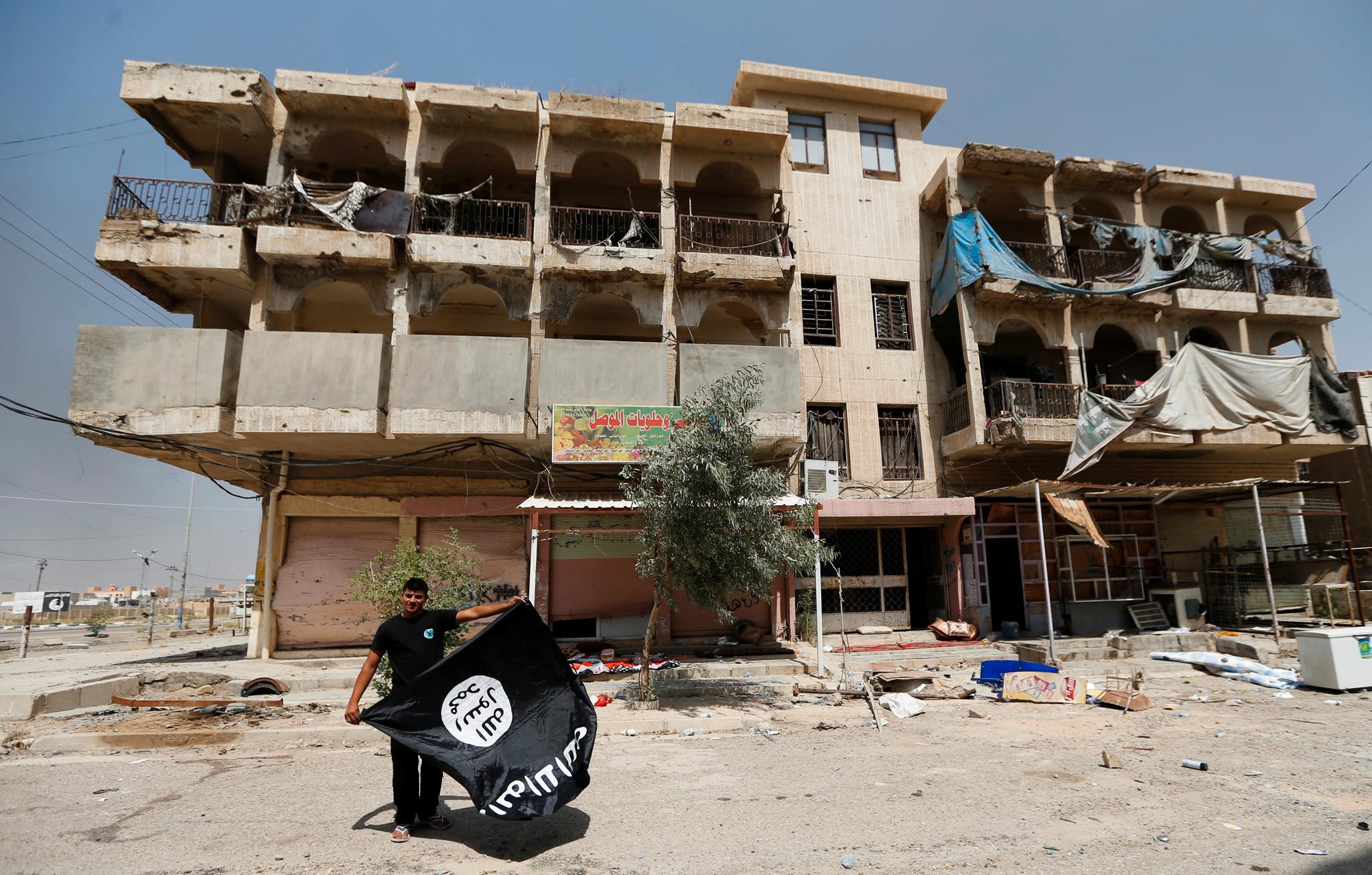 Et medlem av irakiske sikkerhetsstyrker holder et IS-flagg etter å ha tatt det ned fra en bygning i Falluja. Byen hadde 300.000 innbygger før ISIL (senere IS) overtok kontrollen i januar 2014. Nå er store deler av byen fullstendig ødelagt.