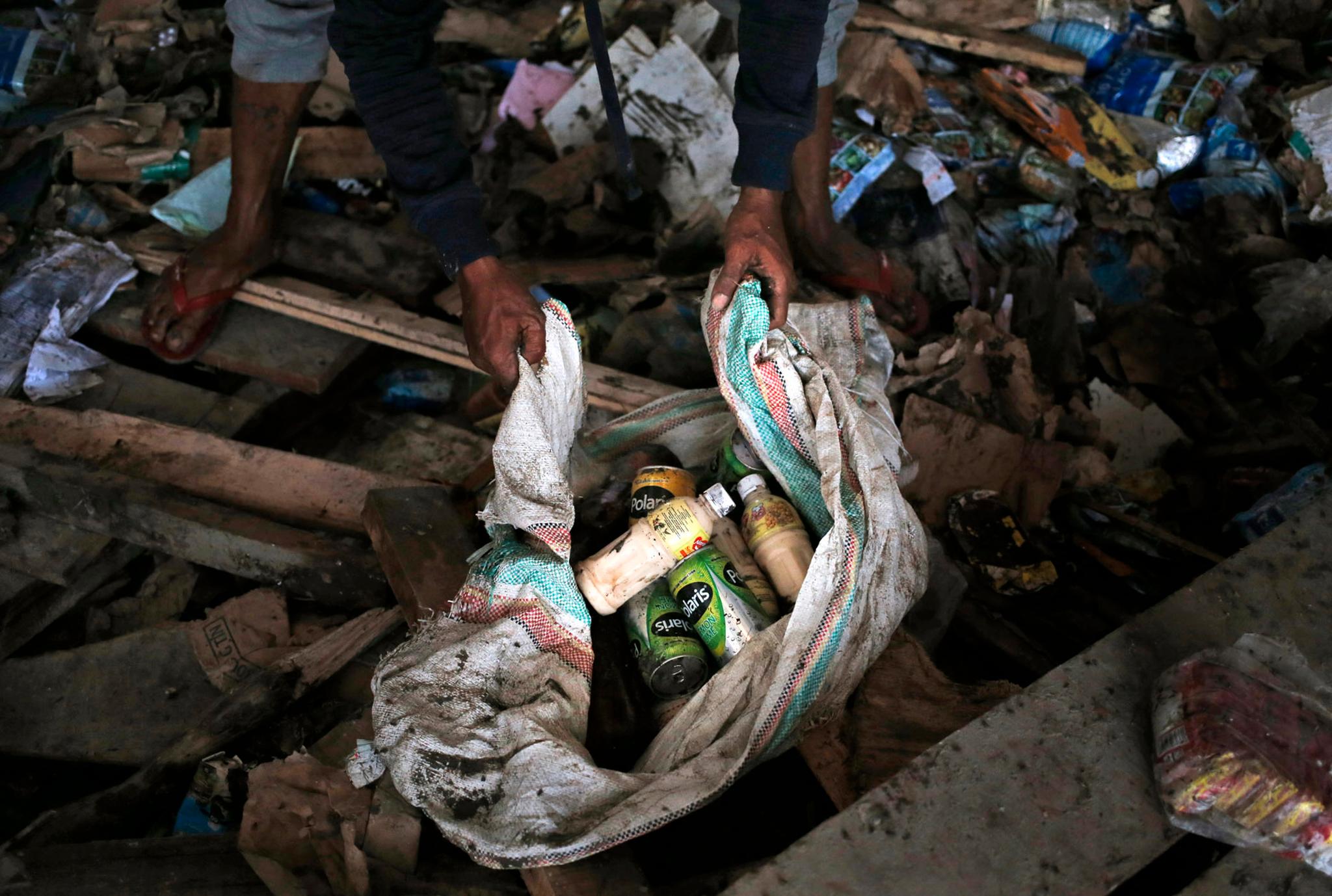En mann samler sammen drikkeflasker fra en ødelagt dagligvarebutikk i  Palu.