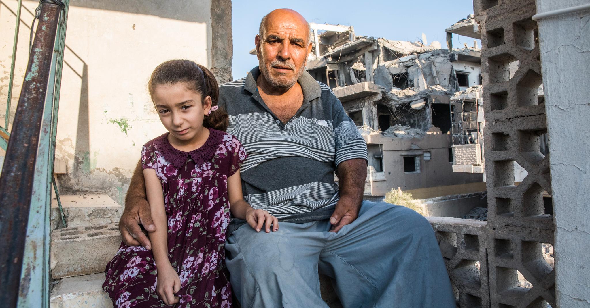 Khaled Abud Hassan og datteren Shahed (8) sitter i trappen i det delvis ødelagte huset deres i Raqqa. Huset ble ødelagt da nabohusene ble bombet av koalisjonen i juni 2017.