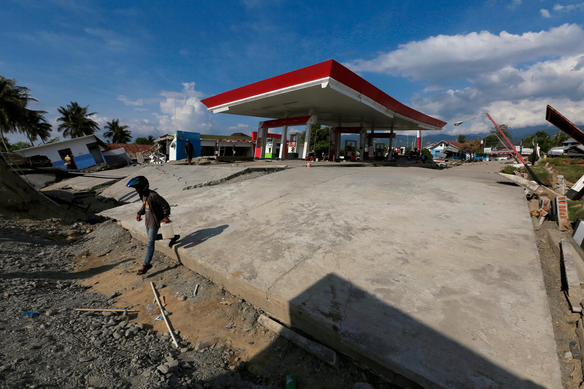 En mann bærer en kanne med bensin fra en ødelagt bensinstasjon i Palu.