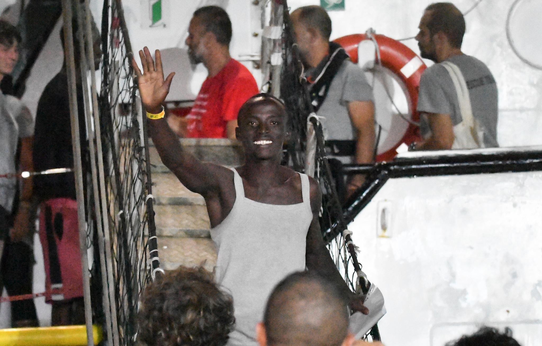 En migrant vinker fornøyd idet han går av Open Arms på Lampedusa sent tirsdag kveld. 
