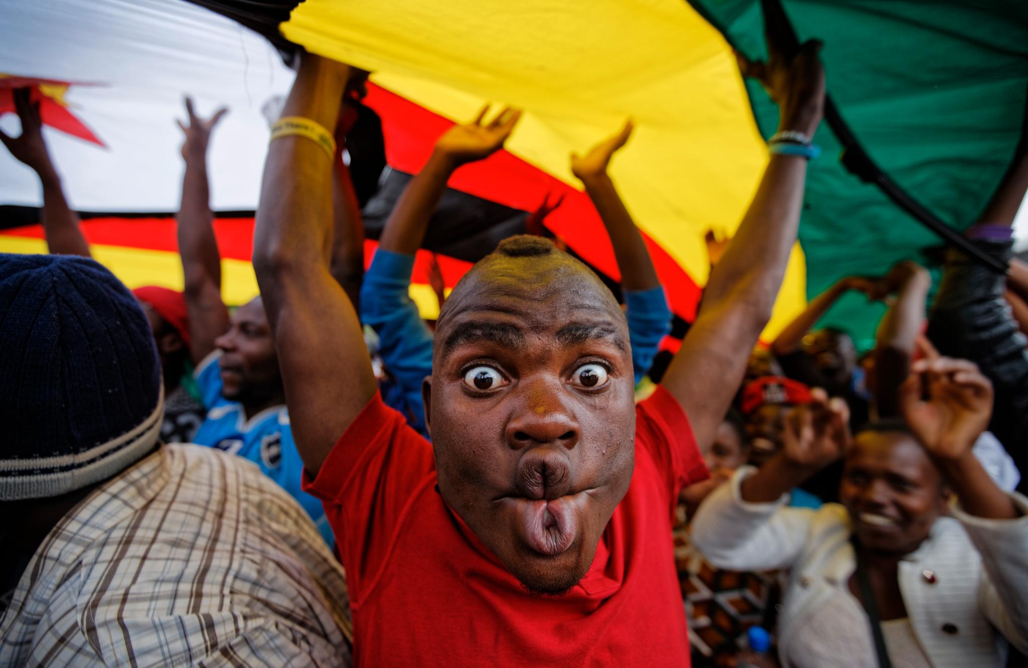 En glad demonstrant i Harare skjærer grimaser mens han står under et stort zimbabwisk flagg lørdag.