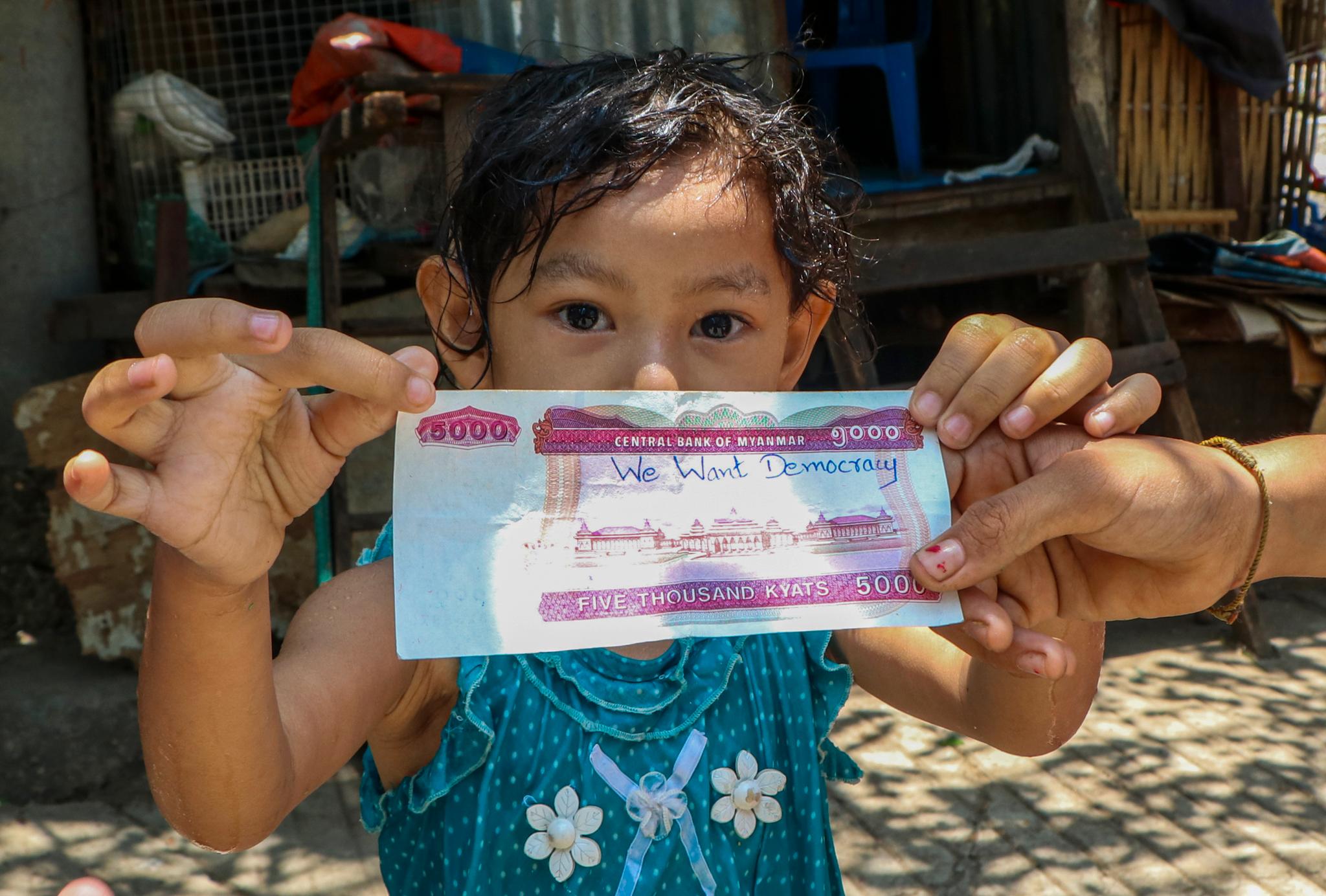 Demonstrantene i Myanmar har funnet mange kreative måter å spre budskapet sitt på. Her holder en jente opp en pengeseddel der noen har skrevet «Vi vil ha demokrati».