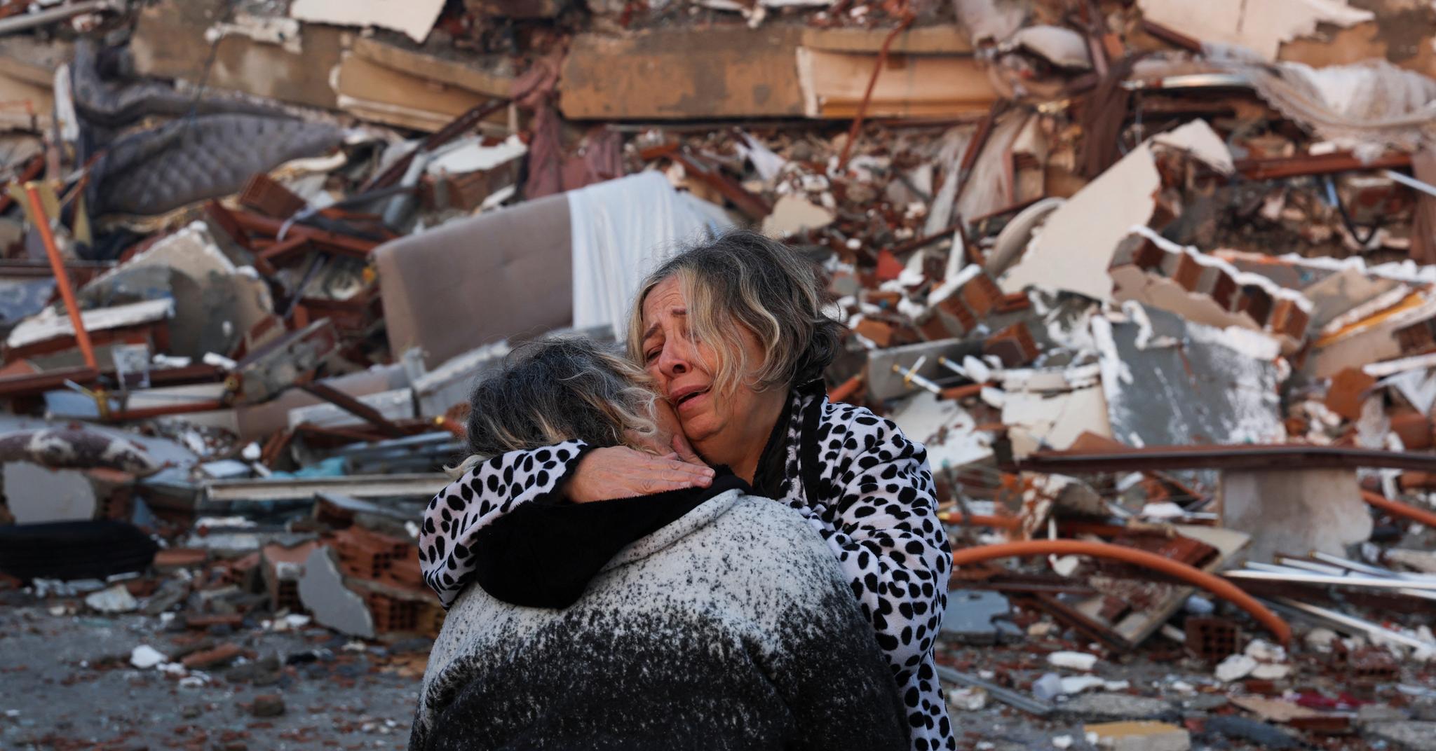 To personer omfavner hverandre i ruinene av ødelagte bygninger i Hatay i Tyrkia. Området har opp gjennom historien vært rammet av mange jordskjelv.