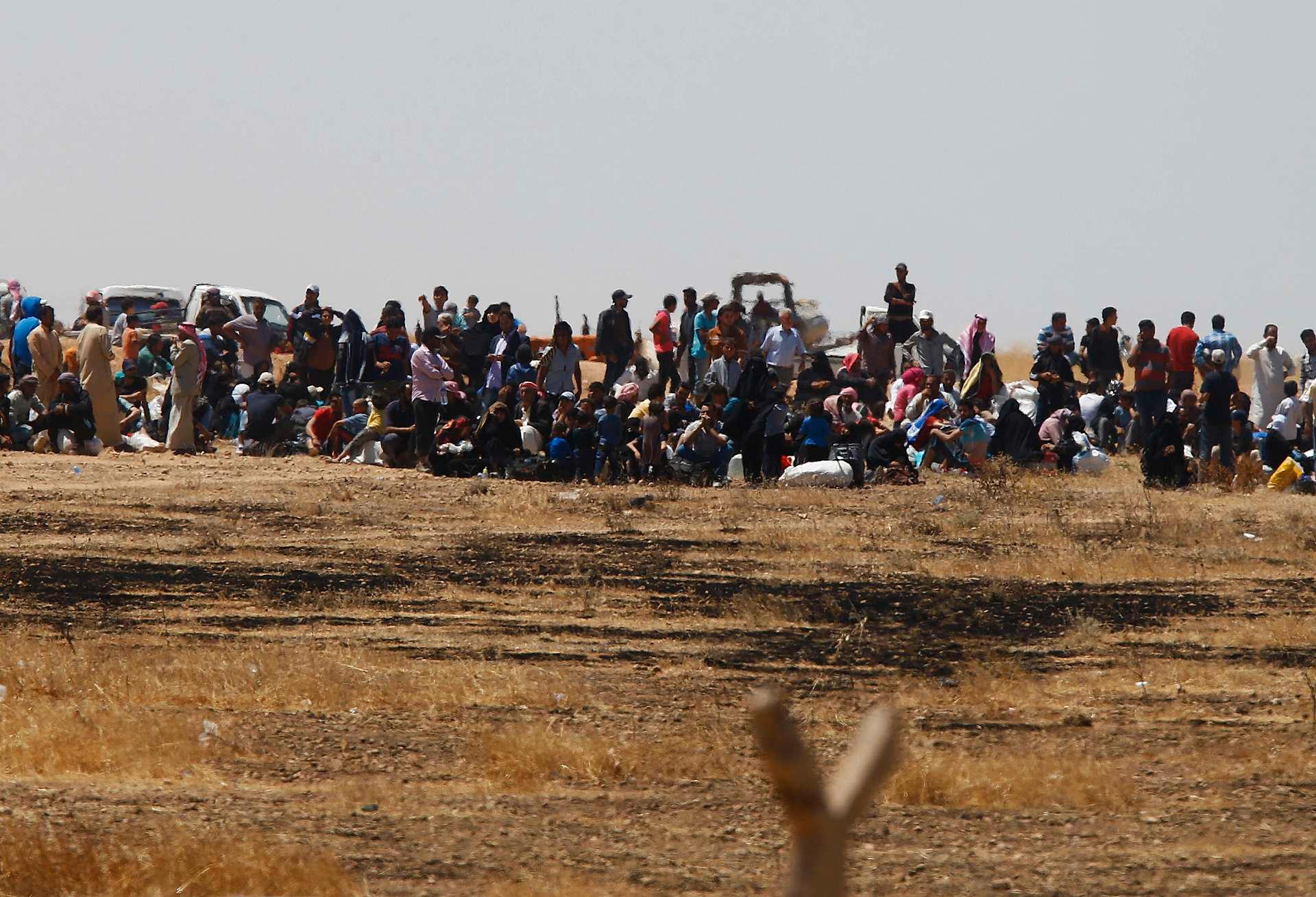 Syriske flyktninger venter nær grensegjerdet mellom Syria og Tyrkia. Flyktningene er avbildet fra den tyrkiske siden av grensen, i nærheten av grenseovergangen Akcakale i Sanliurfa-provinsen - litt lengre øst for området hvor Tyrkia ønsker seg en sikkerhetssone.