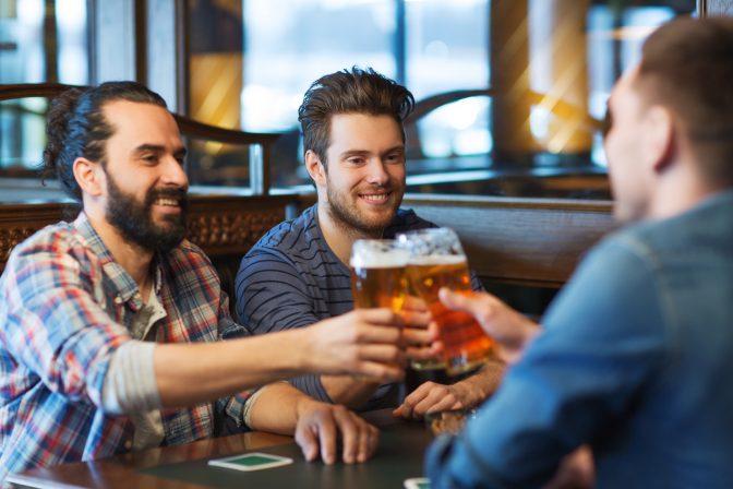 people, men, leisure, friendship and celebration concept - happy male friends drinking beer and clinking glasses at bar or pub