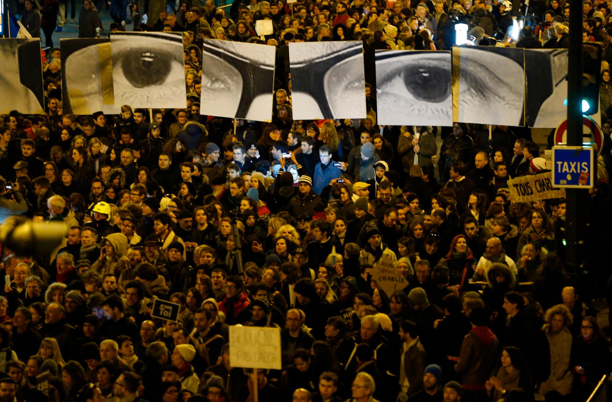 En folkemengde i Paris holder bannere som viser øynene til magasinets avdøde redaktør, Stéphane Charbonnier.