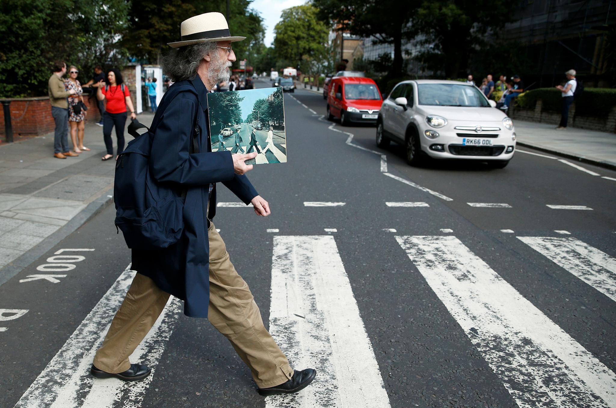 En mann holder det ikoniske fotografiet mens han krysser Abbey Road.  
