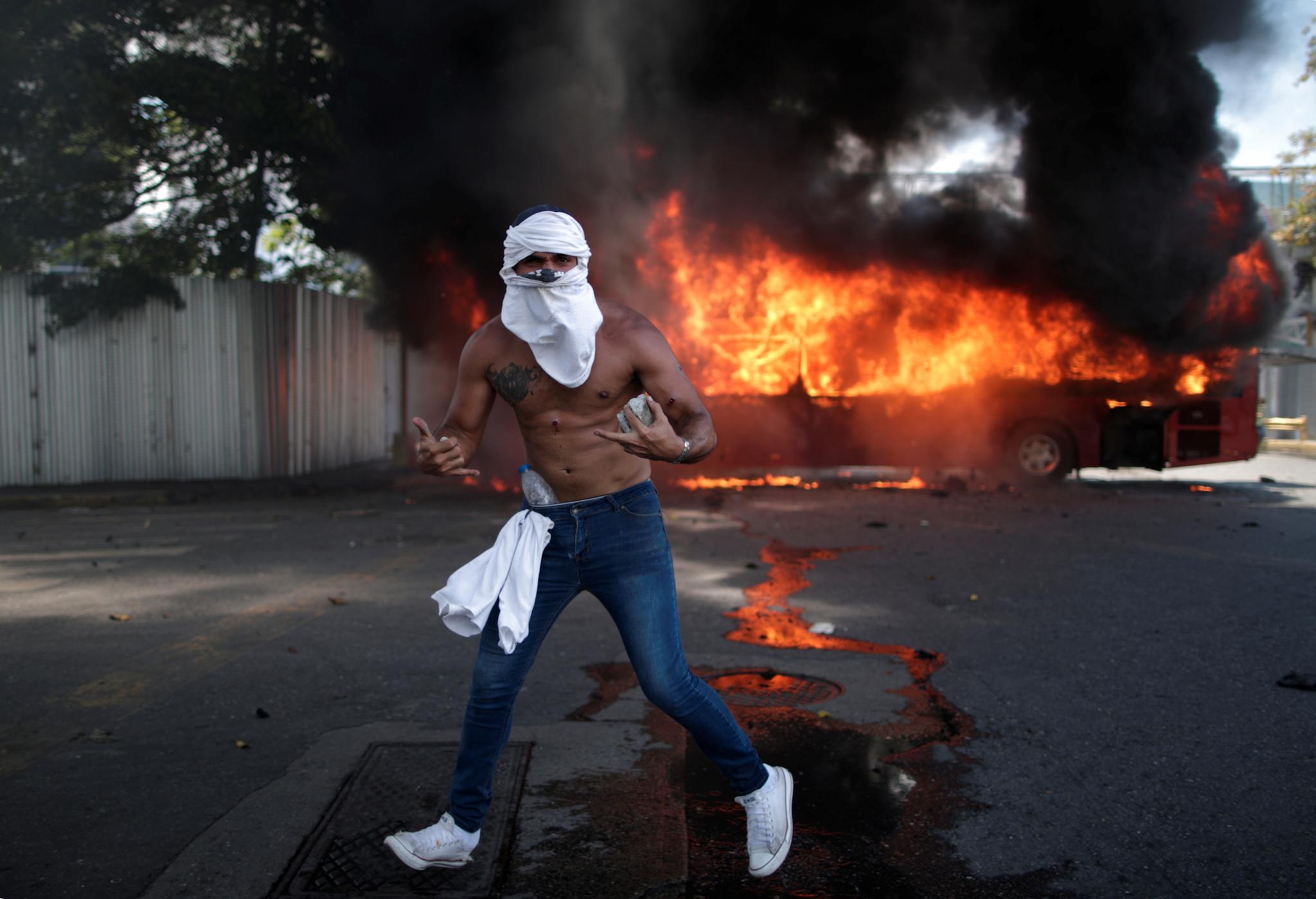 En demonstrant poserer foran en brennende buss nær flybasen La Carlota i Caracas.